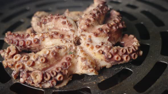 Handheld close up arcing shot of a tender looking cooked octopus on a circular smoking barbeque gril