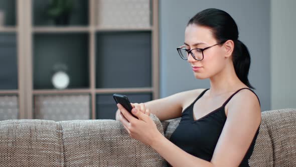 Relaxed Young Brunette Woman Chatting Surfing Internet Use Smartphone Sitting on Comfy Couch