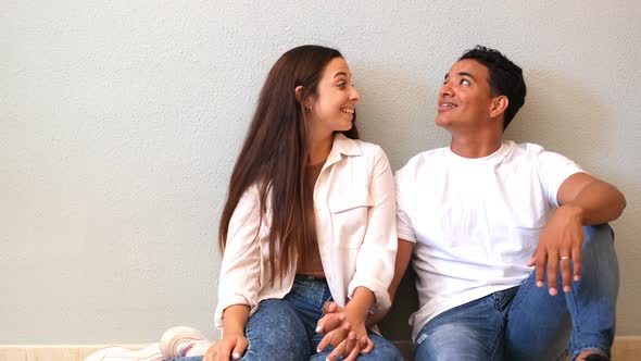 Young couple at home sitting on the floor looking up in to the air and smiling - concept of love