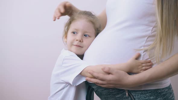 Daughter Hugs Pregnant Mum Belly Standing at Wall in Room