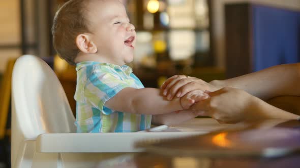 Mom Wipes Her Mouth and Hands at the Adorable Baby. A Charming Child Laughs and Claps