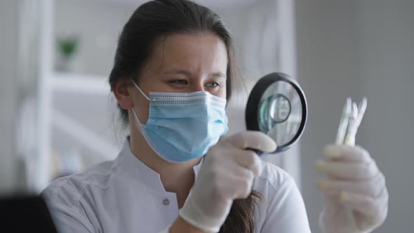 Concentrated Professional Expert Doctor Examining Ampoules with Magnifying Glass Indoors