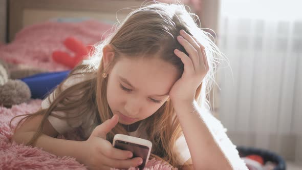 Girl Plays the Phone Lying on the Bed in Her Room