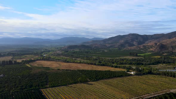 Aerial orbit of green farm fields and tree forest surrounded by mountains on a cloudy day, Cachapoal