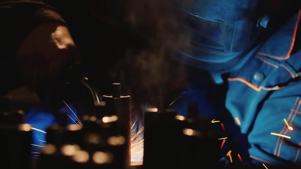 A Welder in a Protective Helmet and Clothes Welds Metal Sparks Illuminate It
