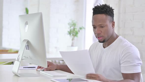 Casual African Man Doing Paperwork with Desktop in Office 