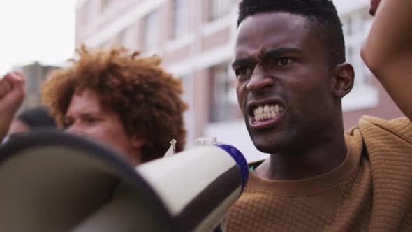 African american man shouting using megaphone with other people raising fists during protest