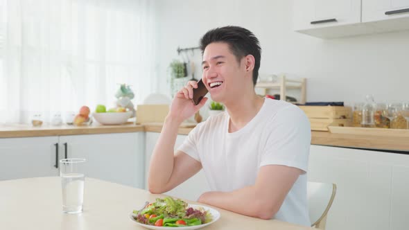 Asian handsome man talk on mobile phone call stand in kitchen at home.