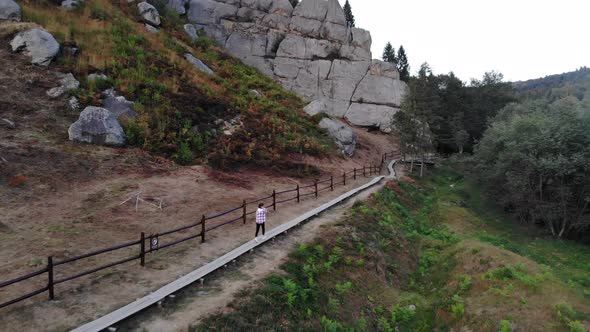 Aerial Top View of Young Tourist Woman Walking on Wooden Trail Between Rocks in National Park of