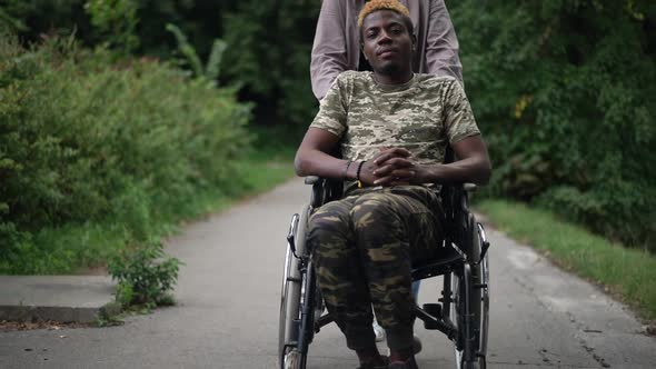 Front View Confident African American Man in Wheelchair with Unrecognizable Caucasian Woman Riding