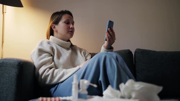 Sick Young Woman Sitting on Sofa Having Video Call with Consult with Doctor at Home