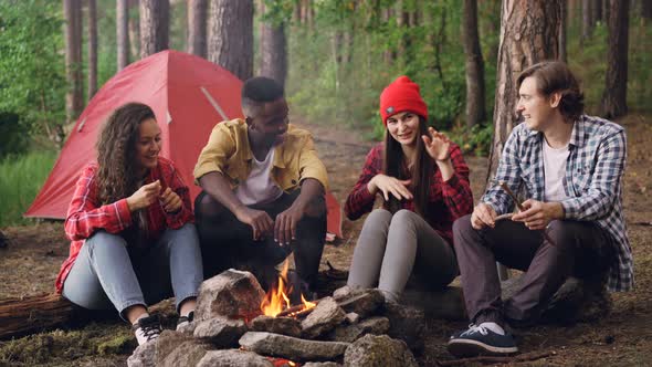 Joyful Tourists Men and Women Are Sharing Stories Sitting Around Campfire and Laughing Getting Warm