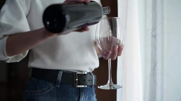 girl pours and drinks wine from a large glass, standing near the window