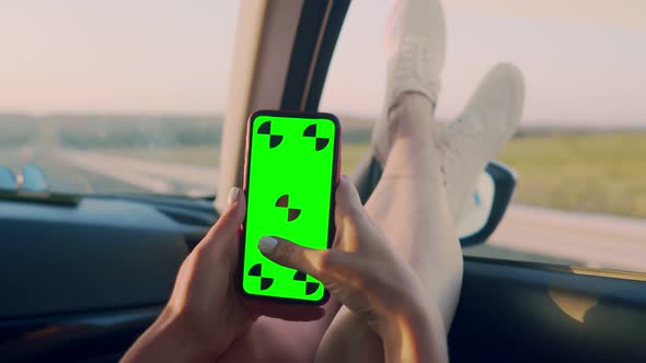 Women's hands hold phone with chromakey while driving in car with their legs out the window.