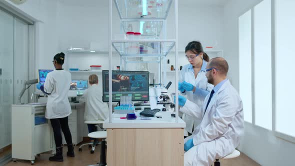 Scientist Coworkers Testing Liquid Using Tube Test and Microscope