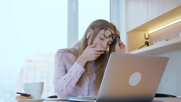 Young woman sitting at an office desk and a laptop yawns and stretches from hard work