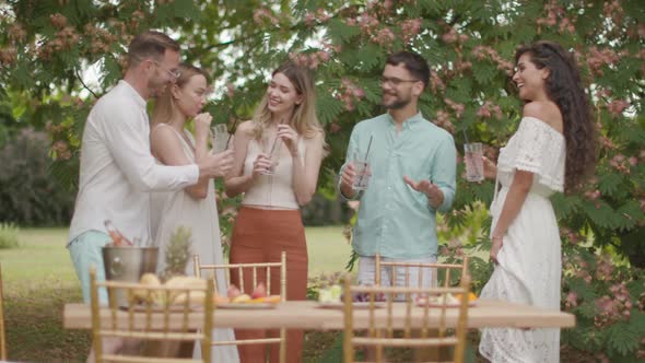  Group of happy young people cheering with fresh lemonade and eating fruits in the garden