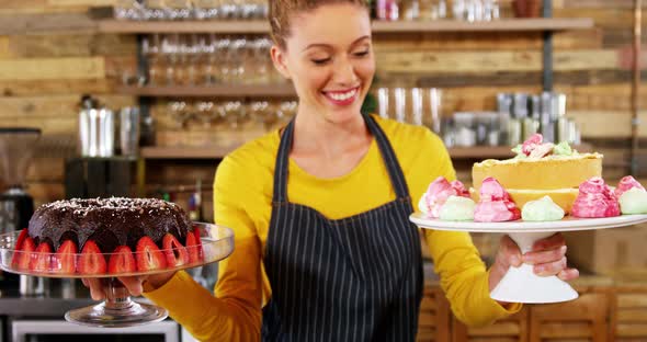 Portrait of waitress holding cake in cake stand at cafe