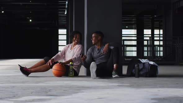 African american man and woman resting after game drinking water and laughing