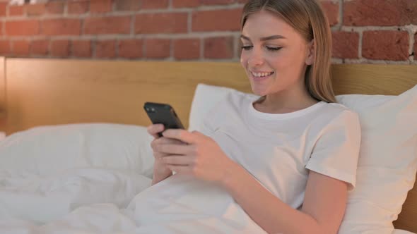 Attractive Young Woman Using Smartphone in Bed 