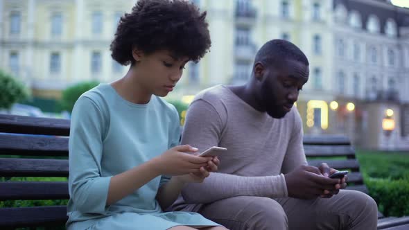 Addicted to Gadgets Young Couple Messaging in Smartphones Sitting on Bench