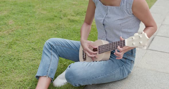 Woman play a song on ukulele at outdoor park