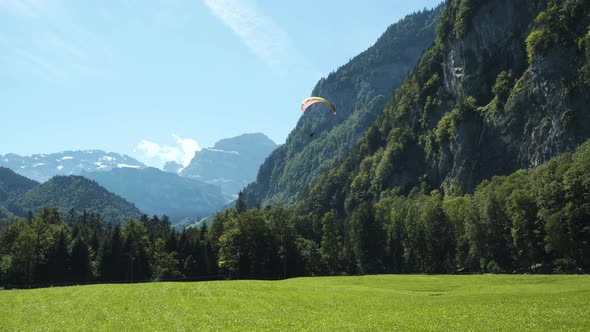 Paraglider flying in the valley, close to the Alps in Switzerland, handheld, wide shot