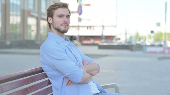 Young Man Smiling at Camera While Sitting on Bench