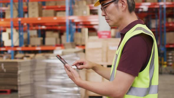 Asian male worker wearing safety suit and using smartphone in warehouse
