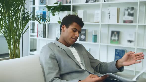 Black Businessman Reading Paper on Sofa. Adult African-American Man in Suit Sitting on Sofa in