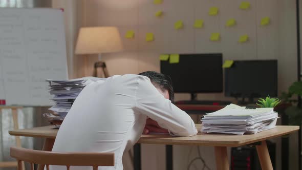 Back View Of Asian Man Sleeping While Working Hard With Documents At The Office