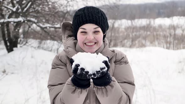 Happy Young Woman Playing with Snow on a Winter Day