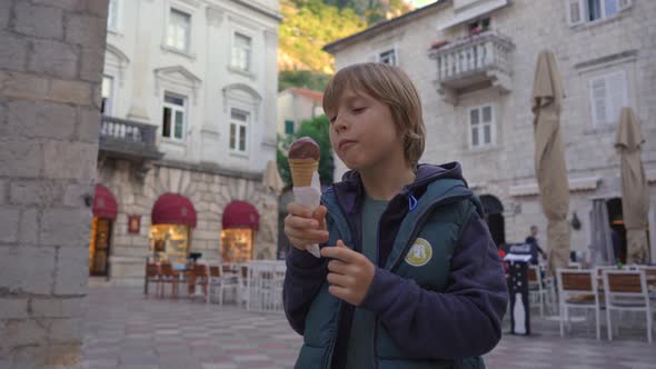 The Little Boy is Eating Chocolate Ice Cream Standing on a Square in the Old Town of Kotor in