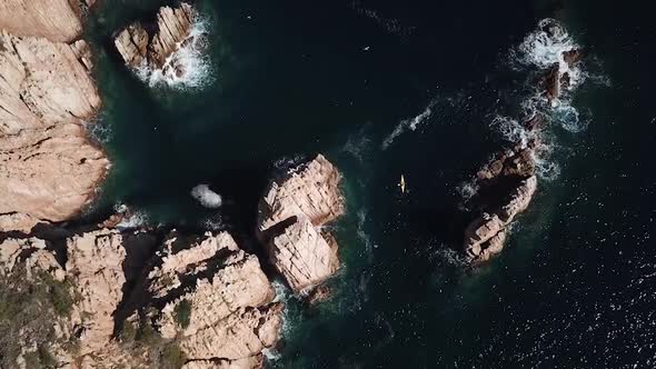 Flying above a kayak between mediterranean rocks, waves and seagulls on a sunny day