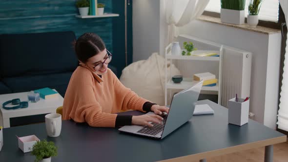 Student Talking on Phone Call and Working on Laptop at Home