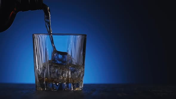 Whiskey Poured in Glass From Bottle at Blue Background with Copyspace at Right