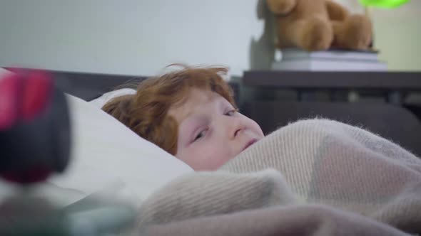 Side View of Little Redhead Caucasian Boy Hiding Under Blanket. Terrified Cute Child Afraid To Be