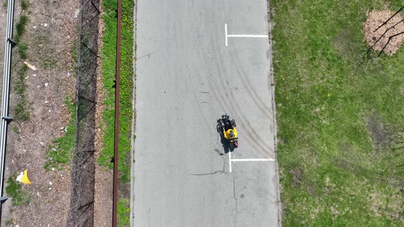 A top down view of a man on a recumbent bicycle, riding in an empty park on a sunny day. The drone c