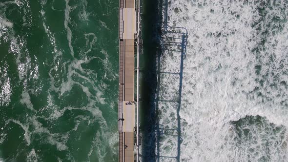 Large waves breaking under a government infrastructure open to the public to use as a walk platform