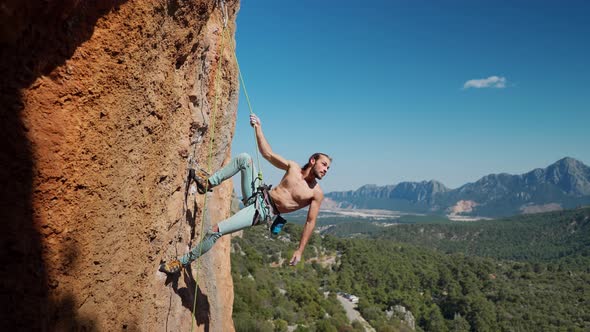 Strong and Muscular Fit Rock Climber Hangs on Rope on Vertical Cliff