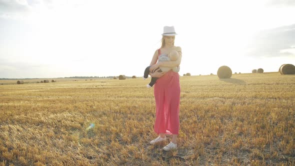 Mother Feeds the Baby Son with Breast in Haystack Field on Horizon with Sunlight
