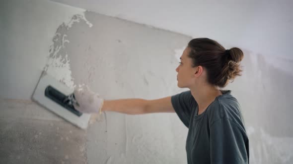 A Professional Repairwoman Puts a Plaster on the Wall with a Spatula