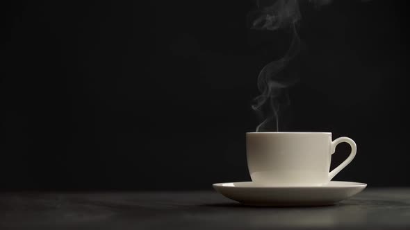Steaming Coffee Cup on Black Background. Puffs of Steam Slowly Coming From a White Cup