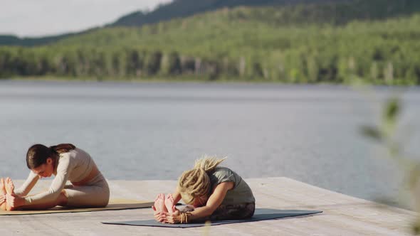 Two Women Practicing Yoga Forward Bend on Lake Pier