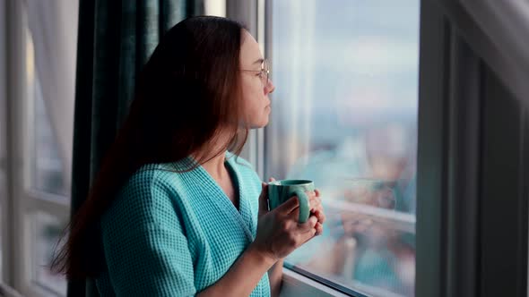 Quarantine in Home Adult Woman is Drinking Hot Tea or Coffee and Looking at Window