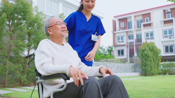 Asian caregiver nurse take care senior male sit on wheelchair outdoor.