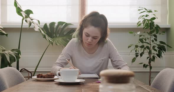 Teen Girl Sitting at Home at Table Writing Lessons Using Smartphone for Learning