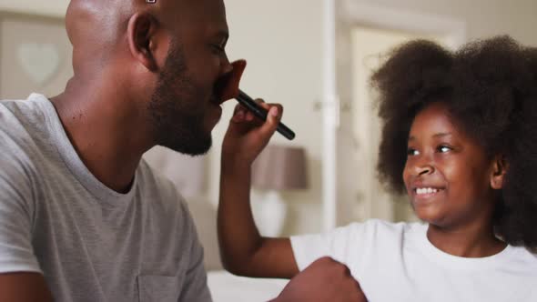 African american girl doing makeup on her father wearing crown at home