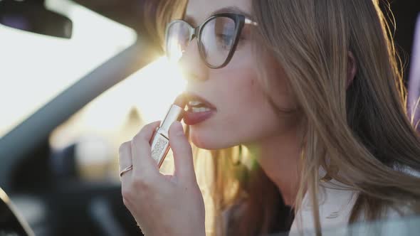 Beautiful Woman Looking in Rear View Mirror and Applying Red Lipstick in Car