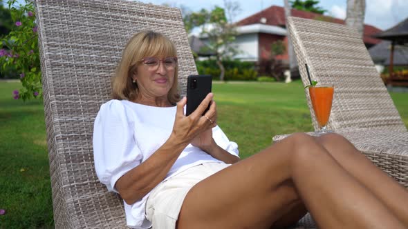 Woman Over 50 on a Sunbed Smiling at Her Smartphone While Video Calling with Beloved Ones